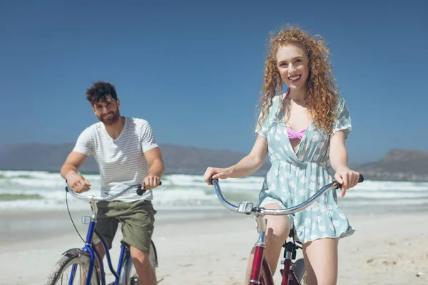 在阳光明媚的日子里 在海滩上骑自行车的年轻白人夫妇的肖像 他们面带微笑 看着镜头 — 图库照片