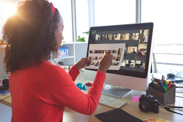 Rear view of beautiful African American female graphic designer looking at photographs at desk in a modern office