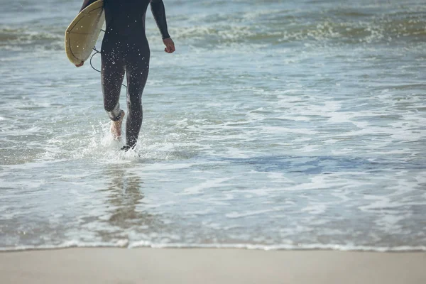 晴れた日のビーチで砂に向かって歩いてサーフボードで男性サーファーの低部は 彼は彼のサーフボードを抱えています — ストック写真