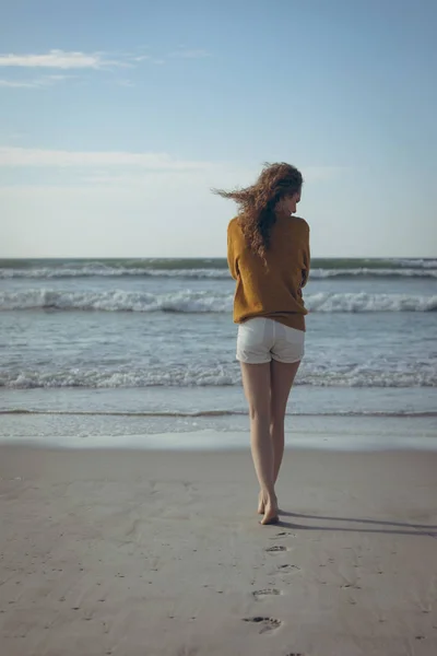 在阳光明媚的日子里 在沙滩上赤脚走在沙滩上的年轻白人妇女的后景 — 图库照片