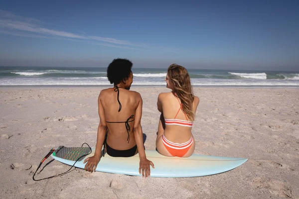 在阳光下 在海滩上 坐在海边冲浪板上的年轻多民族女性的后景 — 图库照片