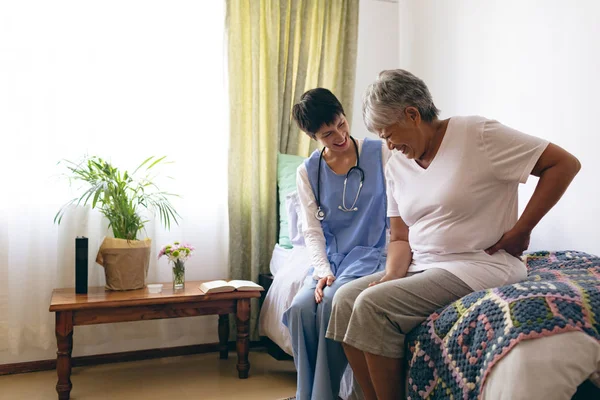 老人ホームで相互に作用するアジア人女性医師と高齢女性患者の側面図 彼女の背中に触れている年配の女性は 痛みを抱えている — ストック写真