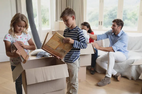 自宅のリビングルームで段ボール箱を開梱する白人家族の正面図 — ストック写真