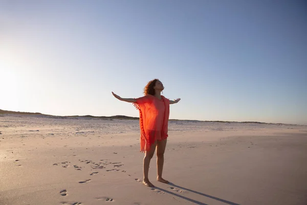 日差しの中で浜辺に立って腕を伸ばした美しい混合レース女性の側面図 — ストック写真