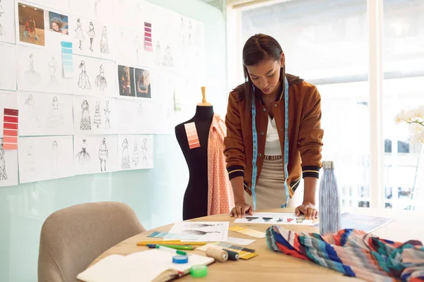 美丽的混血女性时装设计师在现代办公室看桌子上的素描前视图 — 图库照片