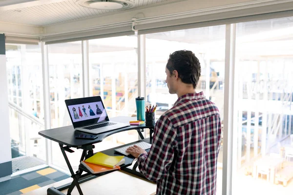 オフィスのデスクでラップトップで作業している白人男性グラフィックデザイナーの背面図 — ストック写真