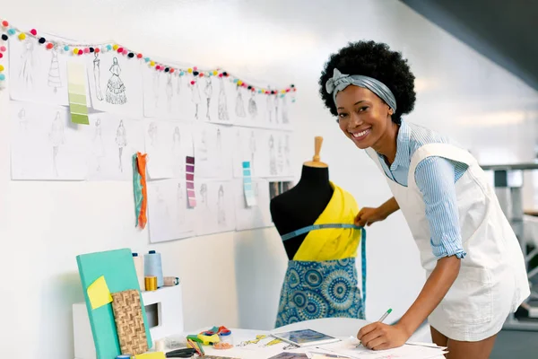 オフィスでマネキンを測定しながら 紙に書く幸せなアフリカ系アメリカ人女性グラフィックデザイナーの側面図 — ストック写真