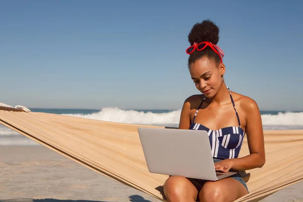 太陽の下のビーチでハンモックでラップトップを使用して美しいアフリカ系アメリカ人女性の正面図 — ストック写真
