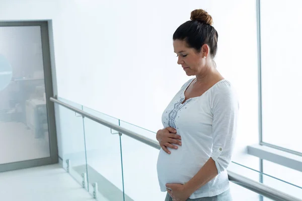 病院の廊下で彼女の腹に触れる白人妊婦の側面図 — ストック写真