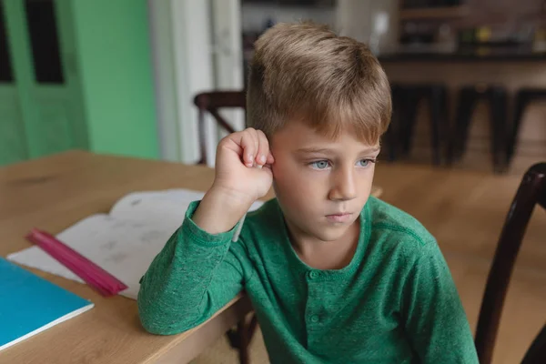 快適な家のダイニングテーブルに座りながら離れて見ているかわいい白人の少年の正面図 — ストック写真