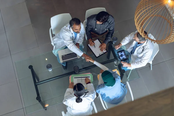 病院のテーブルで一緒に働く多様な医療チームの高い角度の眺め コーヒーカップ 医療用フォルダー クリップボード デジタルタブレット ノートパソコンがテーブルの上にあります — ストック写真