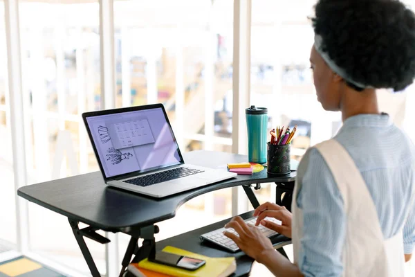 オフィスのデスクでラップトップで作業しているアフリカ系アメリカ人女性グラフィックデザイナーの側面図 — ストック写真