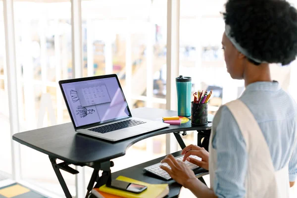 Side view of African american female graphic designer working on laptop at desk in office