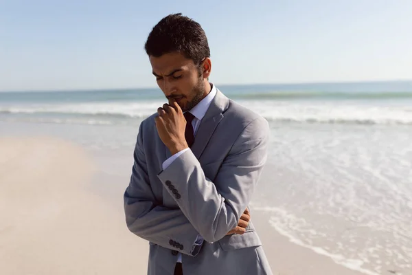 ビーチに立つ思慮深い若い混合人種ビジネスマンの正面図 — ストック写真