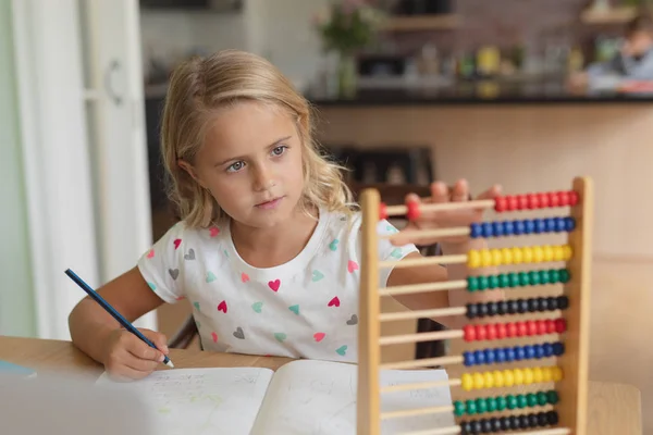 快適な家のテーブルで宿題をしている白人の女の子の正面図 — ストック写真