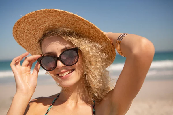 ビーチでカメラを見て帽子とサングラスをかぶった美しい白人女性の正面図 — ストック写真