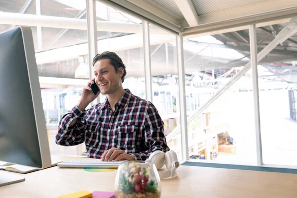現代のオフィスの机で携帯電話で話す幸せな白人男性グラフィックデザイナーの側面図 — ストック写真