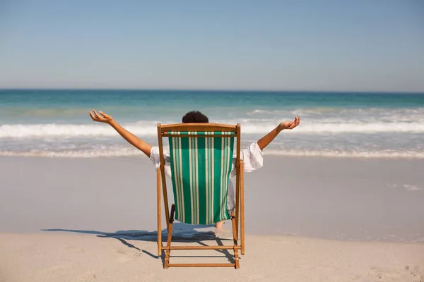 Achteraanzicht Van Afro Amerikaanse Vrouw Met Armen Gestrekt Zittend Strandstoel — Stockfoto