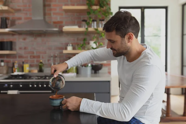 快適な家のダイニングテーブルでコーヒーカップにコーヒーを注ぐ白人男性の側面図 — ストック写真