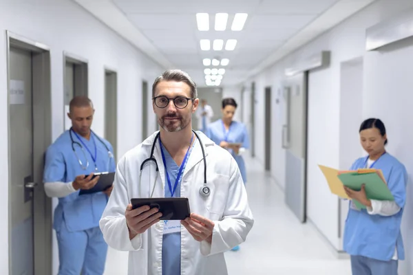 Hastanede Koridorda Dijital Tabletle Ayakta Duran Beyaz Erkek Doktorun Görünümü — Stok fotoğraf
