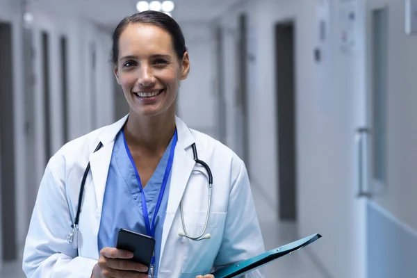 病院の廊下でカメラを見る幸せな白人女性医師の正面図 — ストック写真