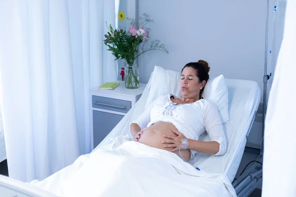 病院の病棟で腹を触りながら痛みに苦しむ白人妊婦の正面図 — ストック写真