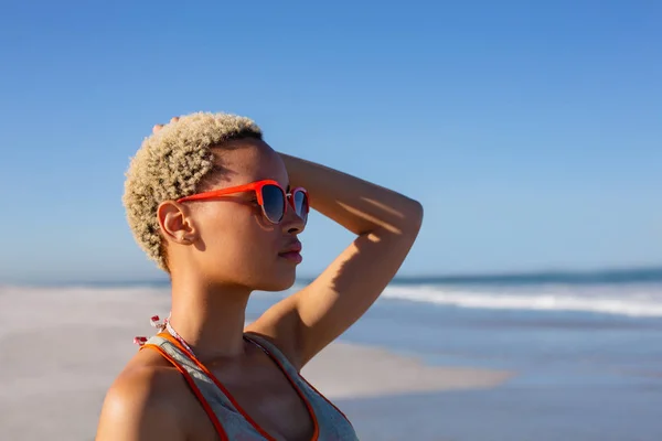 太陽の下でビーチを見下ろすサングラスをかけた美しいアフリカ系アメリカ人女性の側面図 — ストック写真