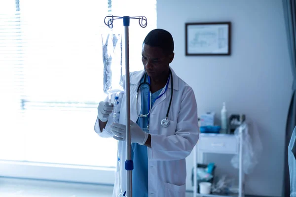 病院の病棟で静脈内治療点滴をチェックするアフリカ系アメリカ人男性医師の正面図 — ストック写真