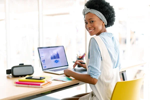 非洲裔美国女平面设计师使用图形平板电脑 同时在办公室办公桌上看笔记本电脑的正面视图 — 图库照片