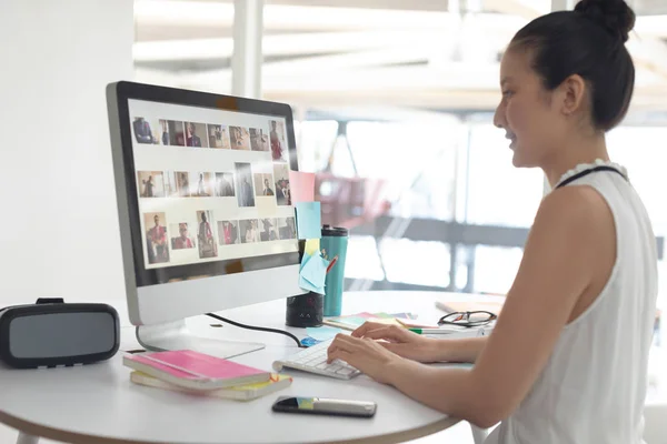 現代のオフィスで机の上でコンピュータに取り組むアジアの女性グラフィックデザイナーの側面図 — ストック写真