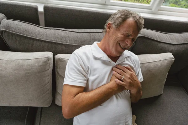 快適な家のソファで胸の痛みに苦しむアクティブな白人男性の高角図 — ストック写真