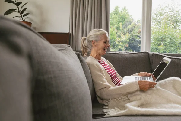 白种人快乐活跃的老年女性在沙发上放松 在舒适的家中客厅里使用笔记本电脑的侧视图 — 图库照片