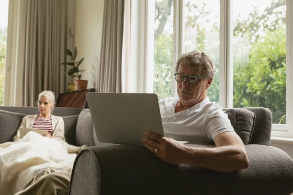 活跃高级白种人男子坐在坐在平板电脑前 而他的妻子在舒适的家里的客厅的平板电脑 — 图库照片
