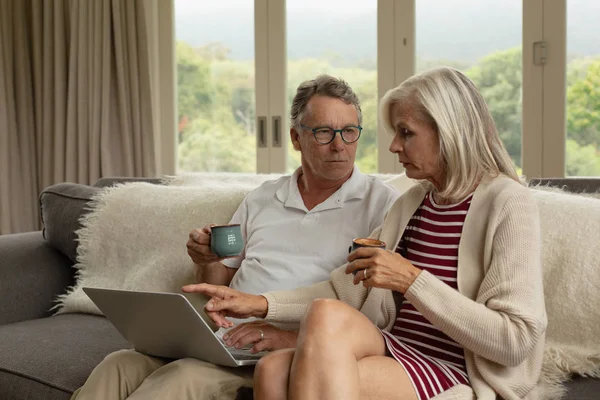 快適な家でソファでコーヒーを飲みながら ラップトップ上で議論するアクティブな白人のカップルの正面図 — ストック写真
