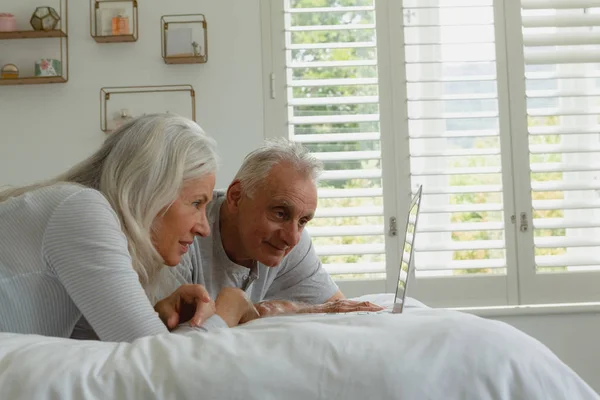 自宅の寝室でベッドに横たわっている間 ラップトップを使用してアクティブな白人のカップルの側面図 — ストック写真