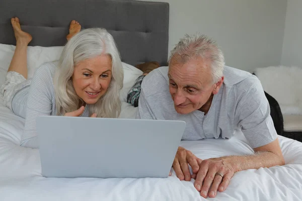 活跃高级白种人夫妇使用笔记本电脑 而躺在卧室的卧室在家里的前视图 — 图库照片