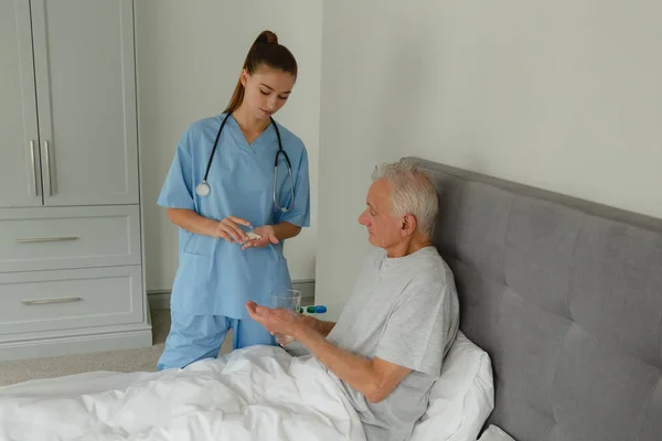 自宅の寝室でアクティブなシニア患者に薬を与える白人女性医師の側面図 — ストック写真