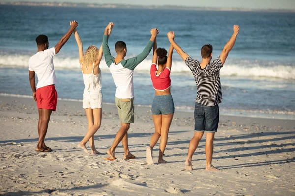 不同朋友站在沙滩上举手的后视图 — 图库照片