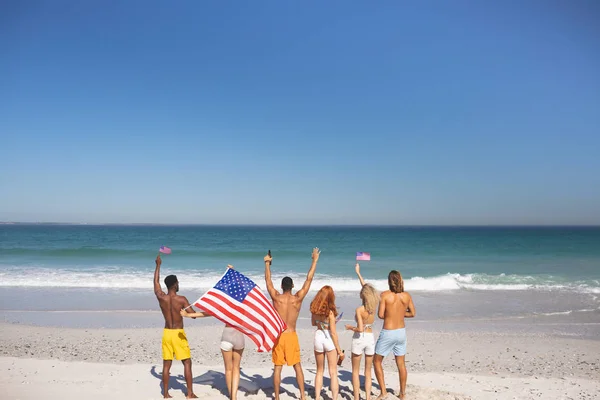 Vista Trasera Una Diversidad Amigos Levantando Las Manos Playa Mientras — Foto de Stock