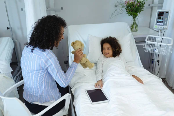 快乐混血母亲在医院病房里展示她的儿子泰迪熊的侧视图 — 图库照片
