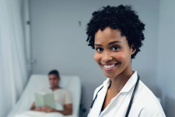 病院の病棟で本を読む混合人種患者の間に微笑むアフリカ系アメリカ人女性医師の肖像 — ストック写真