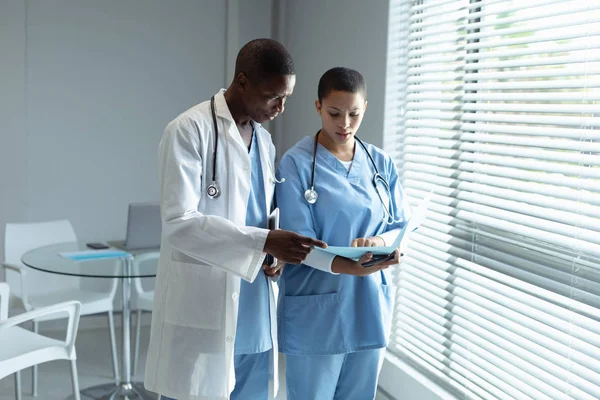病院でファイルを見ているアフリカ系アメリカ人の男性と女性の医師の正面図 — ストック写真
