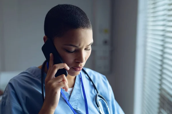 病院で携帯電話で話す若い混合人種女性医師の側面図 — ストック写真