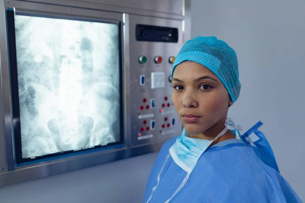 病院のX線ライトボックスの近くに立つ混合人種女性外科医の肖像画 — ストック写真