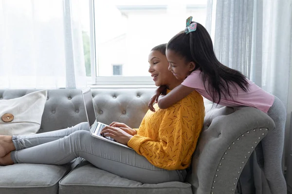 自宅のリビングルームのソファで抱き合うアフリカ系アメリカ人の母と娘の側面図 — ストック写真