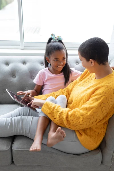 在家中客厅使用数字平板电脑的非洲裔美国人母女侧视图 — 图库照片