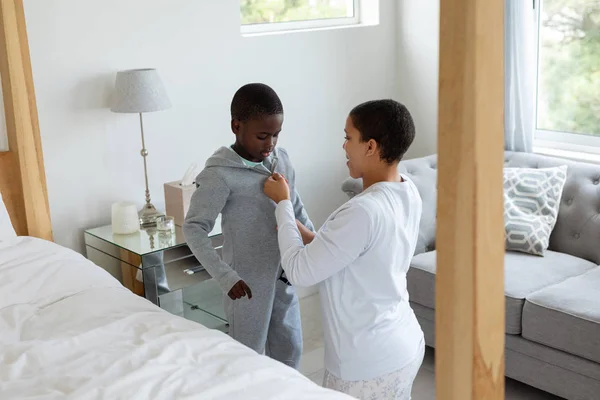 非裔美国人母亲帮助她的儿子在家里的卧室穿衣服的侧视图 — 图库照片