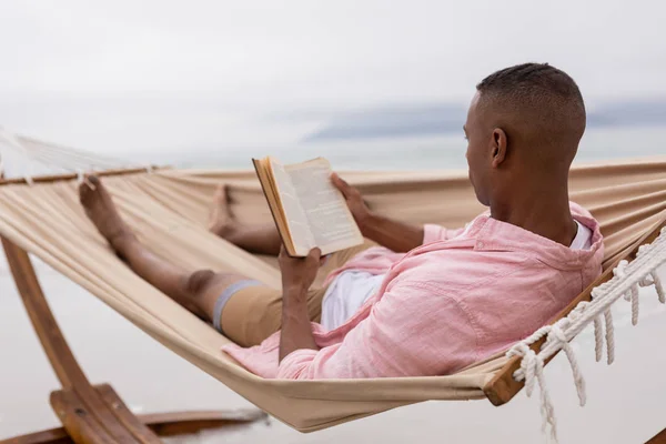 Sahilde Bir Hamakta Dinlenirken Afrikalı Amerikalı Bir Adamın Kitap Okuduğu — Stok fotoğraf