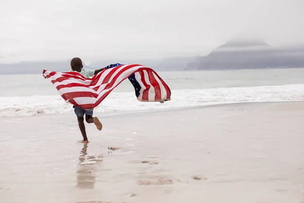 Bakifrån Afroamerikansk Pojke Som Kör Med Amerikanska Flaggan Stranden — Stockfoto