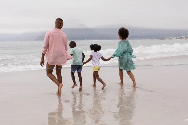 ビーチで手をつないで歩くアフリカ系アメリカ人家族の背面図 — ストック写真